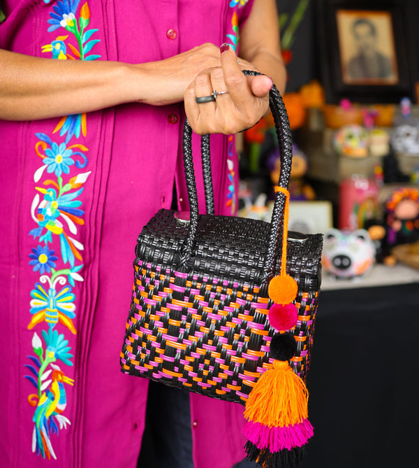 Person holding a colorful woven handbag with tassels against a vibrant background
