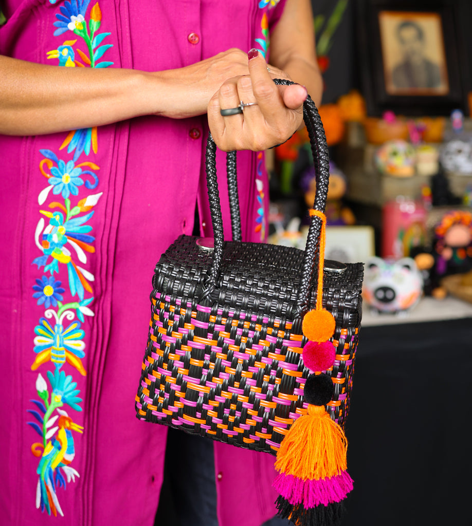 Person holding a colorful woven handbag with tassels against a vibrant background